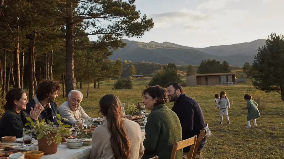 Sakvire neighbors sharing an outdoor table while children play in the meadow